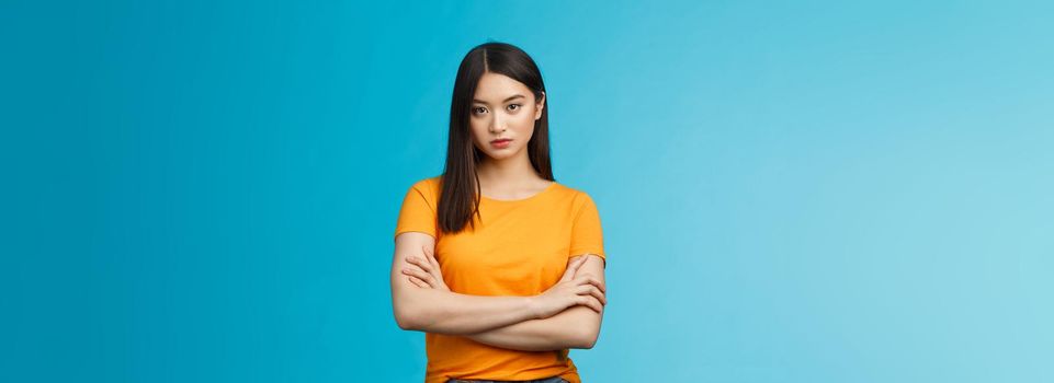 Serious-looking confident and arrogant asian woman cross hands chest powerful ignorant pose, look indifferent strict bored face, stand blue background unimpressed, demand answers. Copy space