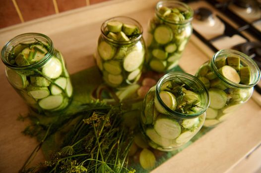 Top view sterilized jars with pickled slices of ripe organic vegetable marrow, marinated in salt or vinegar brine and fresh dill on kitchen table. Food preservation. Canning. Preserving for the winter