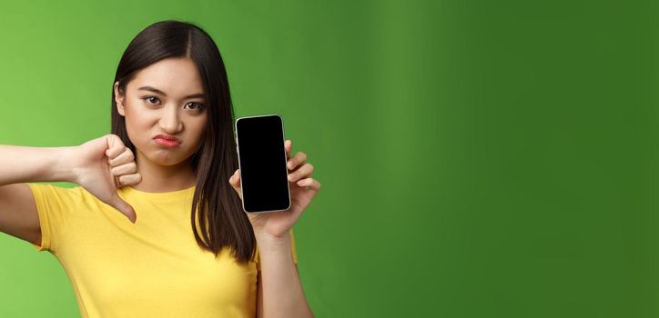 Close-up disappointed upset asian girl judging bad awful app, show smartphone screen, thumb-down grimacing displeased, give negative feedback, cannot stand ex-boyfriend new girlfriend.