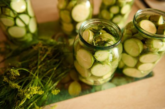 Sterilized glass canning cans with preserved slices of ripe organic vegetable marrow, marinated in salt vinegar brine and fresh dill on the kitchen table. Food preservation. Preserving for the winter