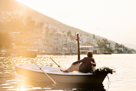 Man and woman sit hugging on the bow of the boat and look at the old town on the seashore. High quality photo