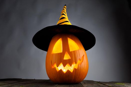 Funny Jack O Lantern Halloween pumpkin wearing witches hat on gray background