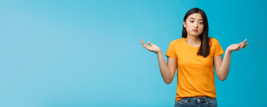 Shit happens. Indifferent absolutely careless female student not care how accident happened shrugging, look camera questioned unaware, hard answer, clueless how deal situation, stand blue background.