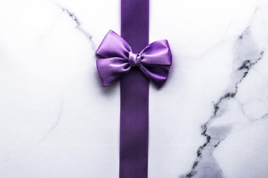 Happy holidays, festive decoration and brand sale promotion concept - Purple silk ribbon and bow on luxury marble background, holiday flatlay backdrop