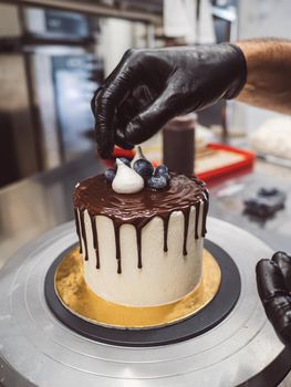 unrecognizable worker preparing a sweet dripping choco cake and berries