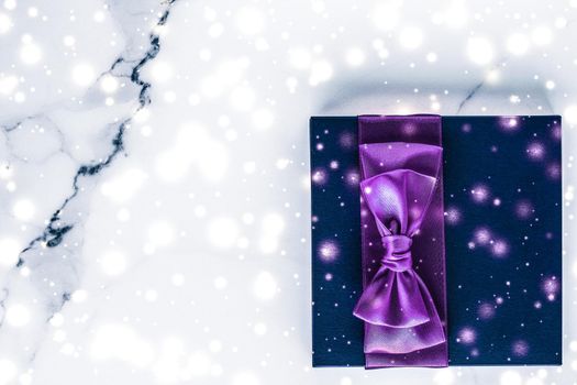 Branding, glamour and cold season concept - Winter holiday gift box with purple silk bow, snow glitter on marble background as Christmas and New Years presents for luxury beauty brand, flatlay design