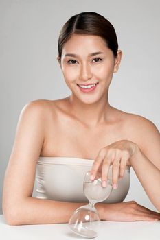 The concept of anti-aging demonstrated by closeup portrait of an ardent young woman holding an hourglass. Skincare treatment, beauty care and cosmetic ideas.