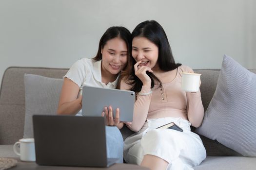 Two asian women having nice lively conversation in living room on sofa in cozy interior.