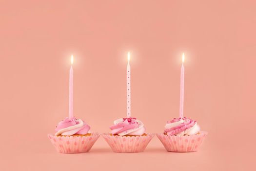 three birthday muffins cupcakes in pink wrappers with pink candles on a pink background high-quality photos for calendar and cards. Space for tex