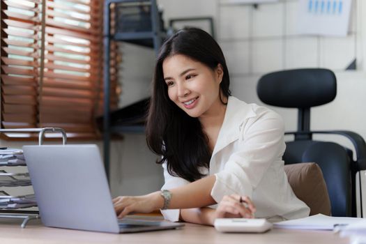 Asian business woman freelancer is working her job on a laptop. Doing accounting analysis report real estate investment data, Financial and tax systems concept.