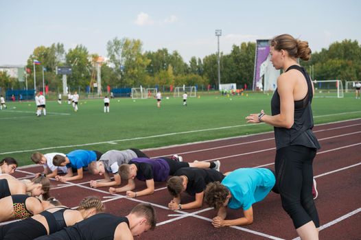 Female coach and group of children conducts a training session at the stadium. School gym trainings or athletics