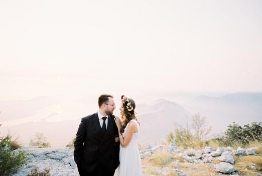 Bride hugs the shoulders of groom, standing on top of a mountain overlooking the Kotor Bay. High quality photo