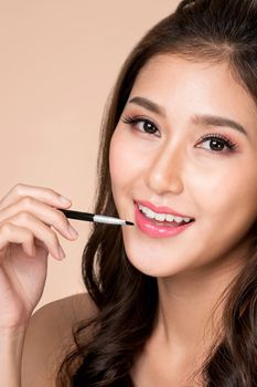 Close up young ardent woman with healthy fair skin applying lipstick on her lip while looking at camera. Beauty concept with cosmetic and makeup.