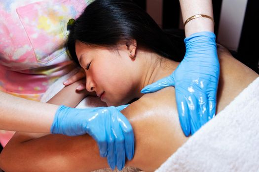 young woman relaxes lying on the beauty salon table while receiving a relaxing shoulder and neck massage, concept of body care and wellness