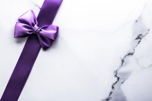 Happy holidays, festive decoration and brand sale promotion concept - Purple silk ribbon and bow on luxury marble background, holiday flatlay backdrop