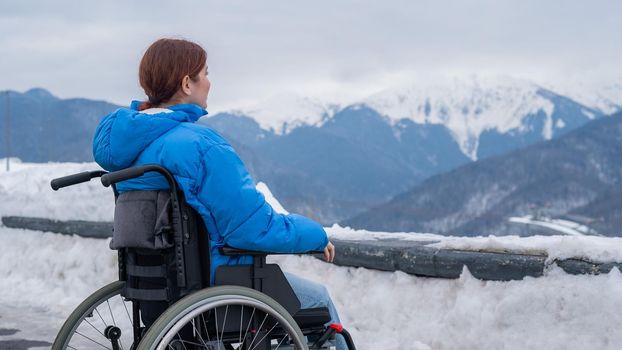 Rear view of a woman in a wheelchair travels in the mountains in winter