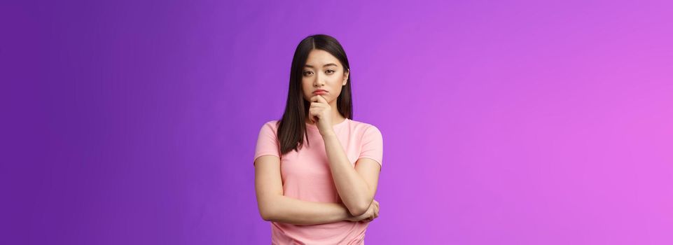 Judgemental serious-looking smart asian girl give expert look, touch chin thoughtful, squinting suspicious uncertain, make decision, choosing product, thinking, pondering plan, purple background.