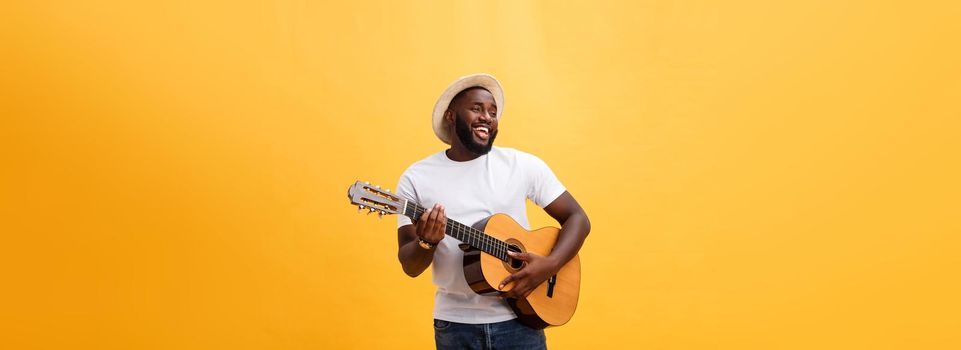 Handsome african american retro styled guitarist playing acoustic guitar isolated on yellow background
