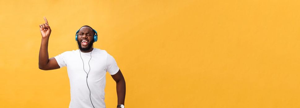 Young African American man wearing headphone and enjoy music dancing over yellow gold Background.