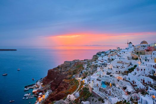 Famous greek iconic selfie spot tourist destination Oia village with traditional white houses and windmills in Santorini island on sunset in twilight, Greece