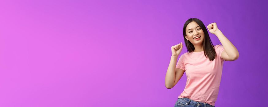 Joyful glamour asian attractive girl having fun enjoy awesome party feeling carefree, fist pump during dance, smiling broadly like good music, attend concert, stand purple background. Copy space