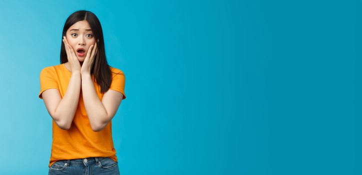 Shocked concerned young asian girl look empathy camera, gasping open mouth worried, frowning upset hear frustrating news, pitty feel sorry for friend, touch cheeks speechless, stand blue background.