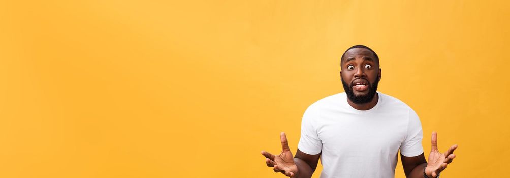 Portrait of african american man with hands raised in shock and disbelief. Isolated over yellow background