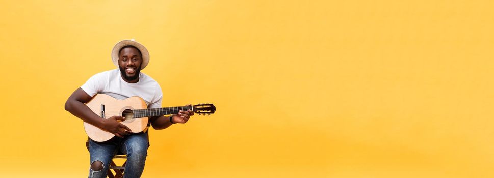 Muscular black man playing guitar, wearing jeans and white tank-top. Isolate over yellow background