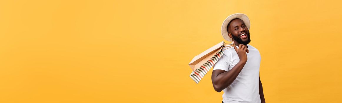 Happy african american man holding shopping bags on yellow background. Holidays concept.