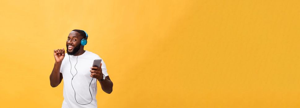 African American man with headphones listen and dance with music. Isolated on yellow background.