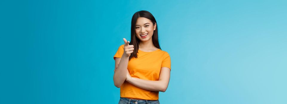 Hey you got point. Cheerful cute asian lively girl dark short haircut pointing camera finger-pistol smiling broadly, encourage friend make move, congratulate coworker good job, stand blue background.