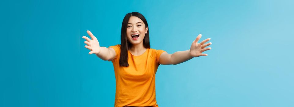 Come closer let me hug you. Cheerful lovely asian brunette girl stretch hands forward wanna cuddle, embracing friend smiling broadly inviting dear guests welcoming, stand blue background.