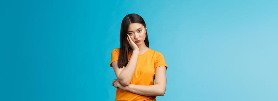Sad bored asian female student attend boring uninteresting lecture lean face palm, look indifferent express apathy dislike, grimacing and sulking disappointed stand blue background bothered.