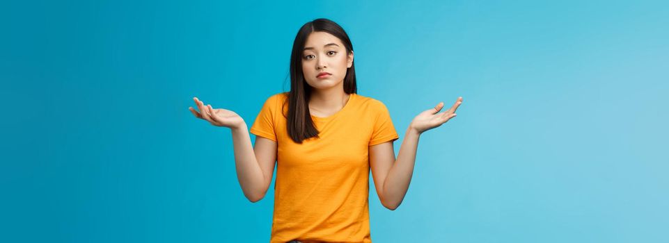 Shit happens. Indifferent absolutely careless female student not care how accident happened shrugging, look camera questioned unaware, hard answer, clueless how deal situation, stand blue background.