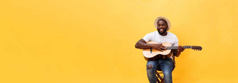 Handsome african american retro styled guitarist playing acoustic guitar isolated on yellow background