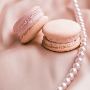 Girly, bakery and branding concept - Sweet macaroons and pearls jewellery on silk background, parisian chic jewelry, French dessert food and cake macaron for luxury confectionery brand, holiday gift