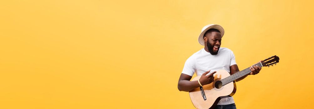 Muscular black man playing guitar, wearing jeans and white tank-top. Isolate over yellow background