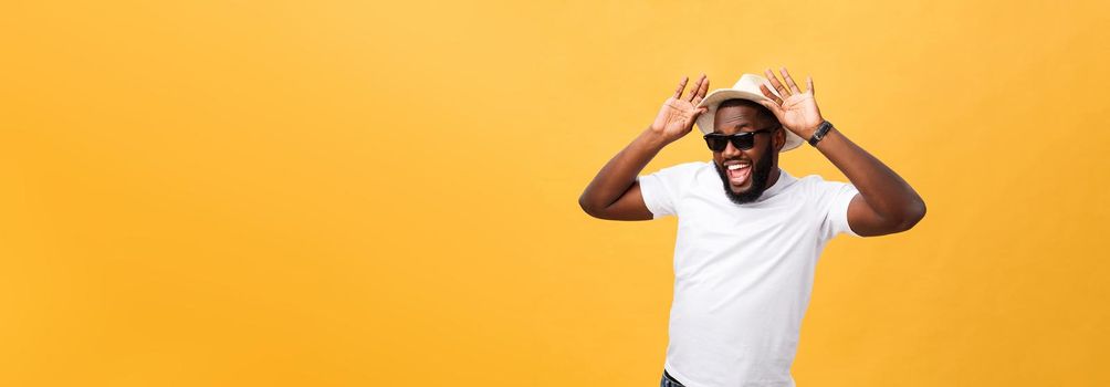 Close up portrait of a young man laughing with hands holding hat isolate over yellow background.