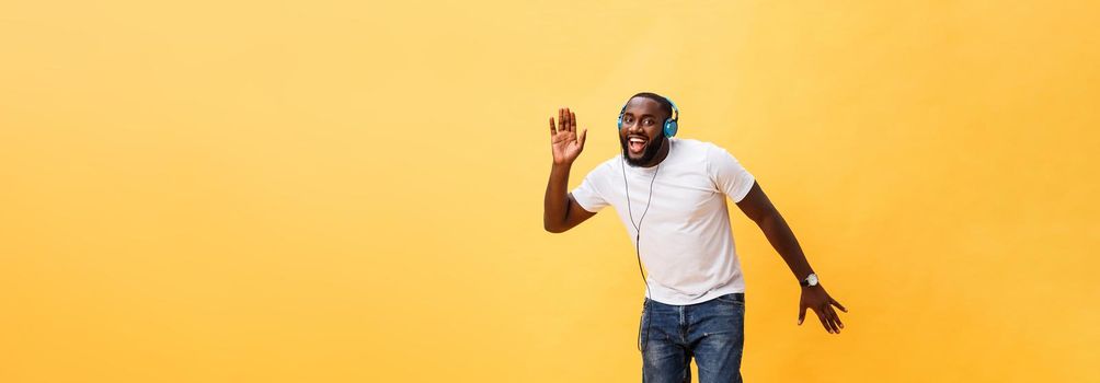 Full length portrait of a cherry young african american man listening to music with headphones and dancing isolated over yellow background.