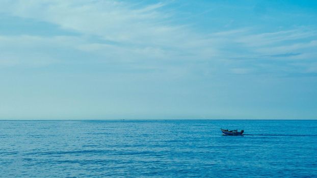 Simple background Calm dark blue sea fishing boat alone white pale Spindrift clouds Open way no limitations.