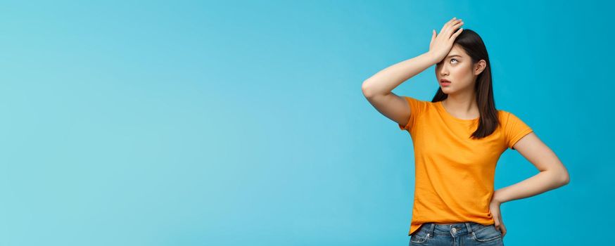 Annoyed arrogant asian girl punch forehead make facepalm sign, roll eyelids irritated pissed, cannot stand lame talks look disappointed ingorant, unwilling to listen, stand blue background.