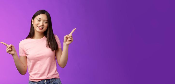 Charismatic relaxed cute asian woman short haircut pointing sideways introduce variety choices, showing left and right products, smiling joyfully, easily making decision, stand purple background.