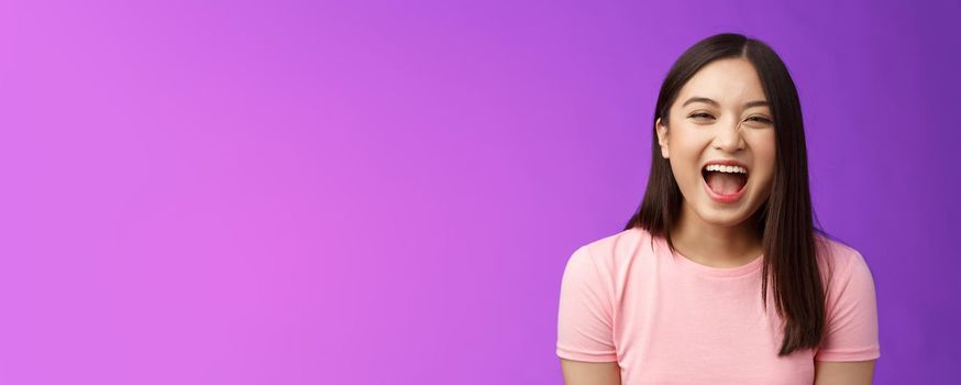 Close-up sincere carefree asian brunette laughing out loud, enjoy comedy movie, having fun, joking friends, stand entertained purple background amused, express positive emotions. Copy space