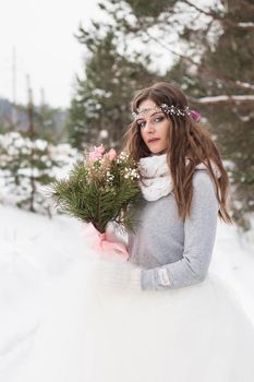 Beautiful bride in a white dress with a bouquet in a snow-covered winter forest. Portrait of the bride in nature.