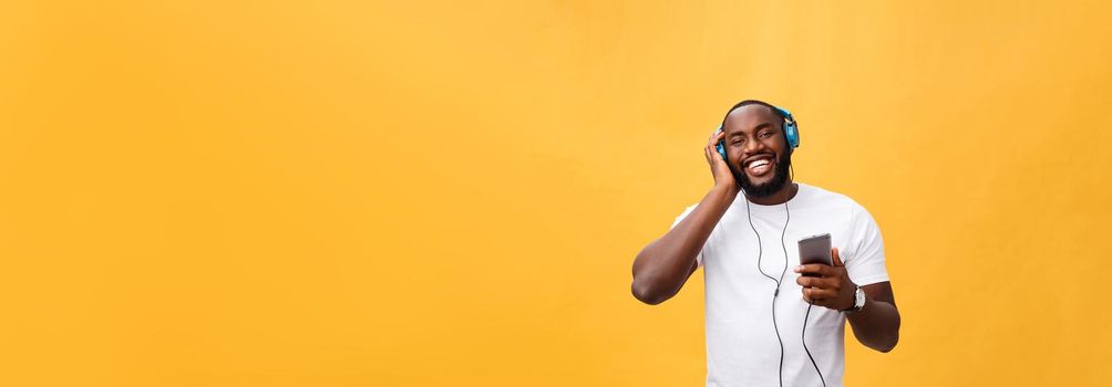 Young African American man wearing headphone and enjoy music over yellow gold Background.