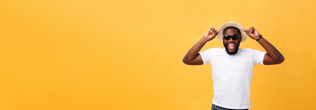 Close up portrait of a young man laughing with hands holding hat isolate over yellow background.