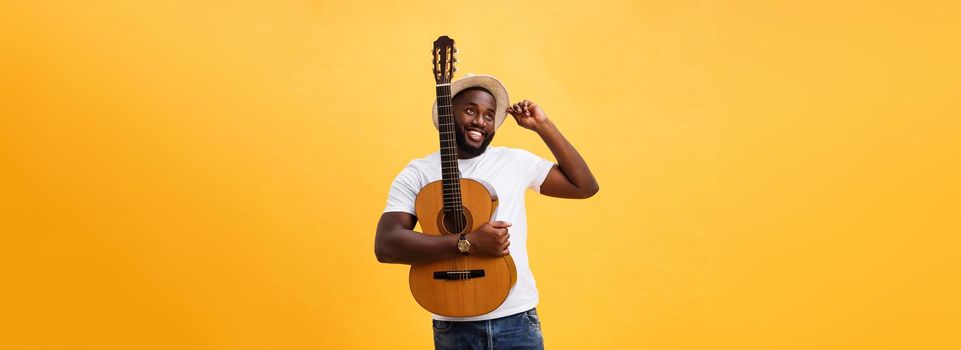 Muscular black man playing guitar, wearing jeans and white tank-top. Isolate over yellow background