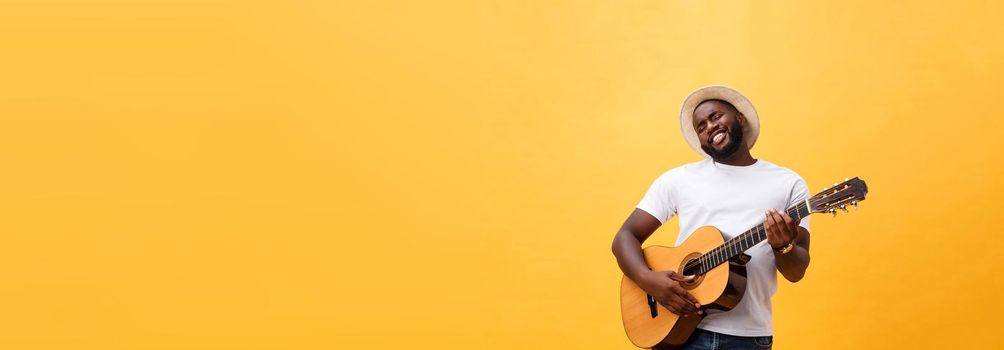 Muscular black man playing guitar, wearing jeans and white tank-top. Isolate over yellow background