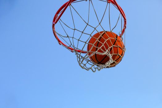 A basketball in a net against the sky. Sports, street game. The ball is in the ring. Hitting the target. Conceptual. Winning competitions. Success. Achieving the goal