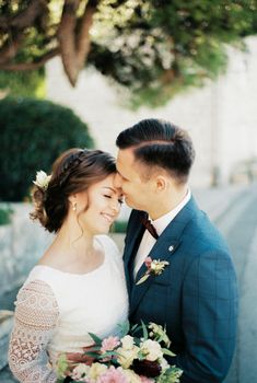 Groom hugs bride by the waist and kisses her forehead. Portrait. High quality photo